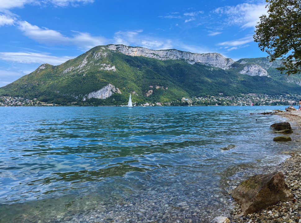 little pebbled beach along the clear water of Lake Annecy with mountain range in the background