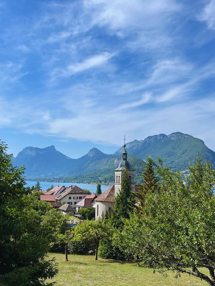 church tower and houses with lake annecy and mountains in the background