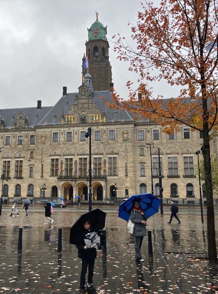 mother and son standing in the rain with an umbrella in front of a old big building in Rotterdam