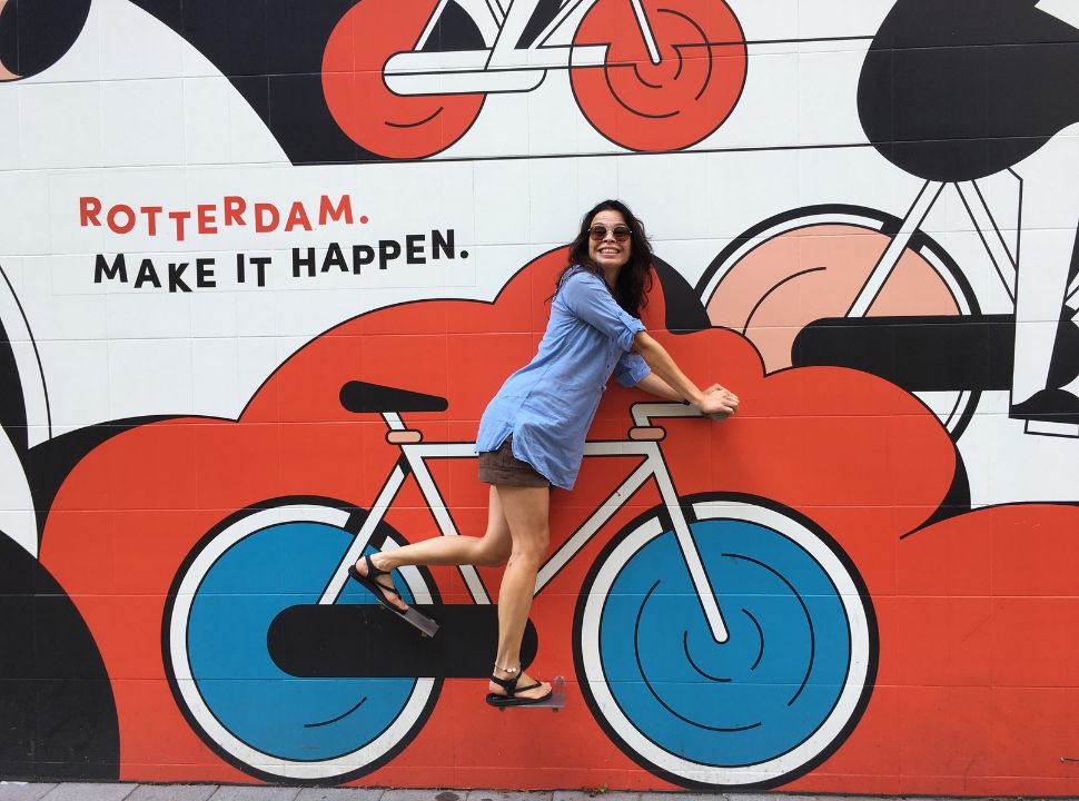 woman standing on peddles of a bike mural with the text rotterdam make it happen