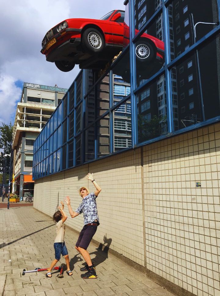 father and son standing under a falling car which is fastened to a building