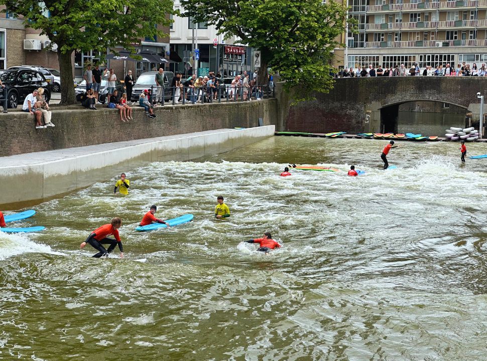 surfers surfing in a canal in rotterdam that creates artificial waves