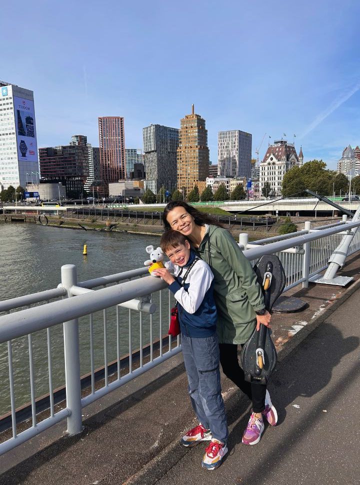 mother and son crossing a bridget with background view of high rise buildings of rotterdam