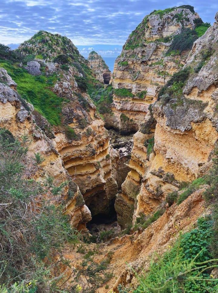 high rock formations with a deep cave covered with green vegetation seen along the hike to ponta da piedade