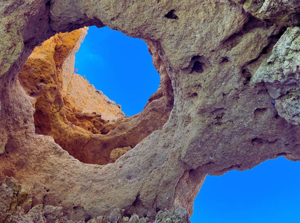 looking up into the blue sky through a hole in the rock formation during a tour to ponta da piedade