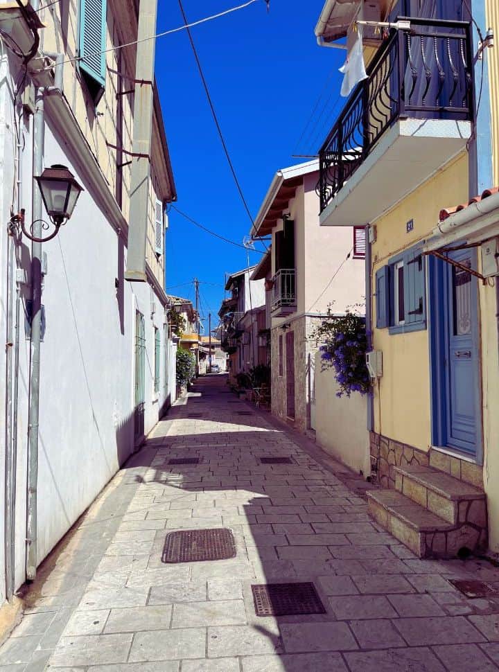 White walls, yellow building with blue door and shutters and other colourful houses in the distance at one of the many narrow streets at Lefkada Old Town