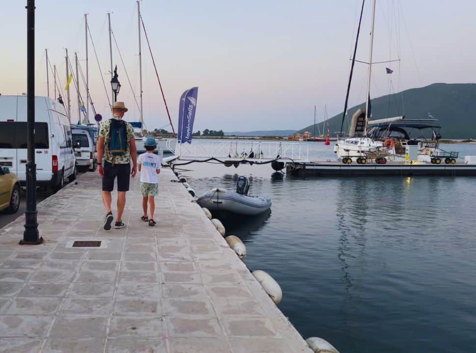 Father and son walking along the walkway at the Lefkada marina with a sail boat docked for the evening