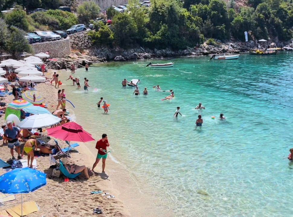 busy little beach with clear turquoise water, very busy with people sitting right at the shoreline