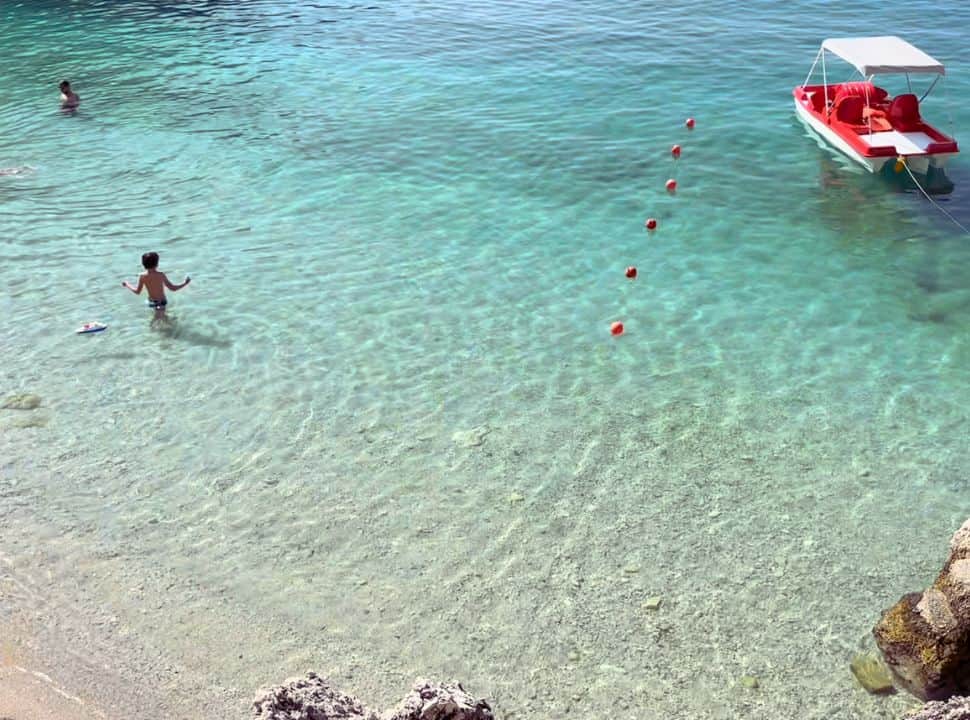 turquiose clear water with a paddle boat and a boy playing with his toy boat at Afteli beach Lefkada