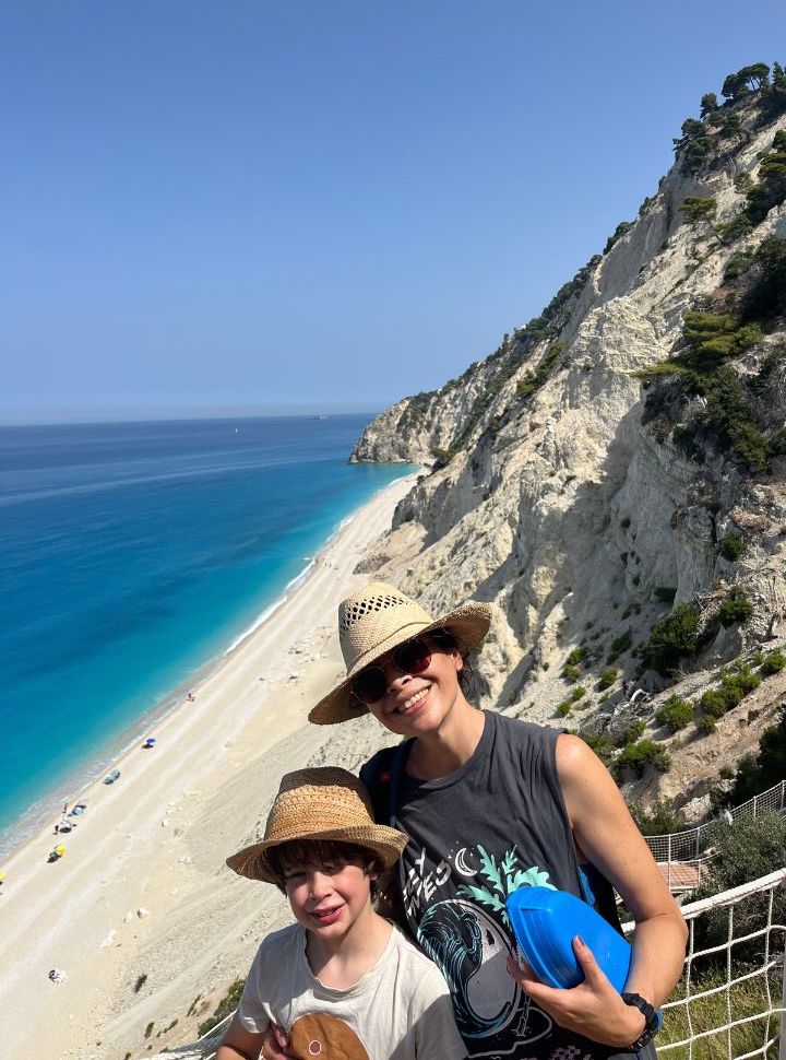 mother and son posing at the stairs leading to Egremni beach. The background shows the white sanded beach, white cliffs and stunning blue water