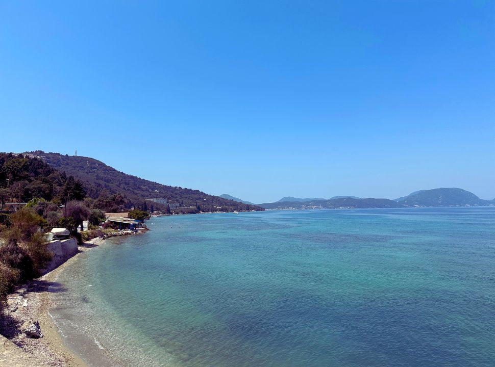 view of a beachfront with accommodation at the water front in south east Corfu, the ocean has various shades of blue and green. 