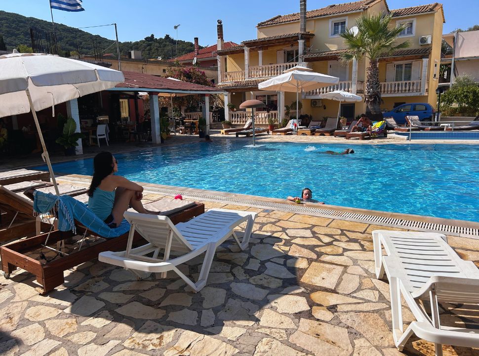 Woman sitting in the shade at the hotel pool while her son plays in the water