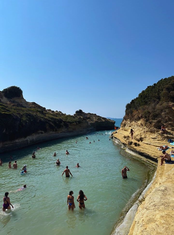 people swimming the ocean water that flows between to cliffs.