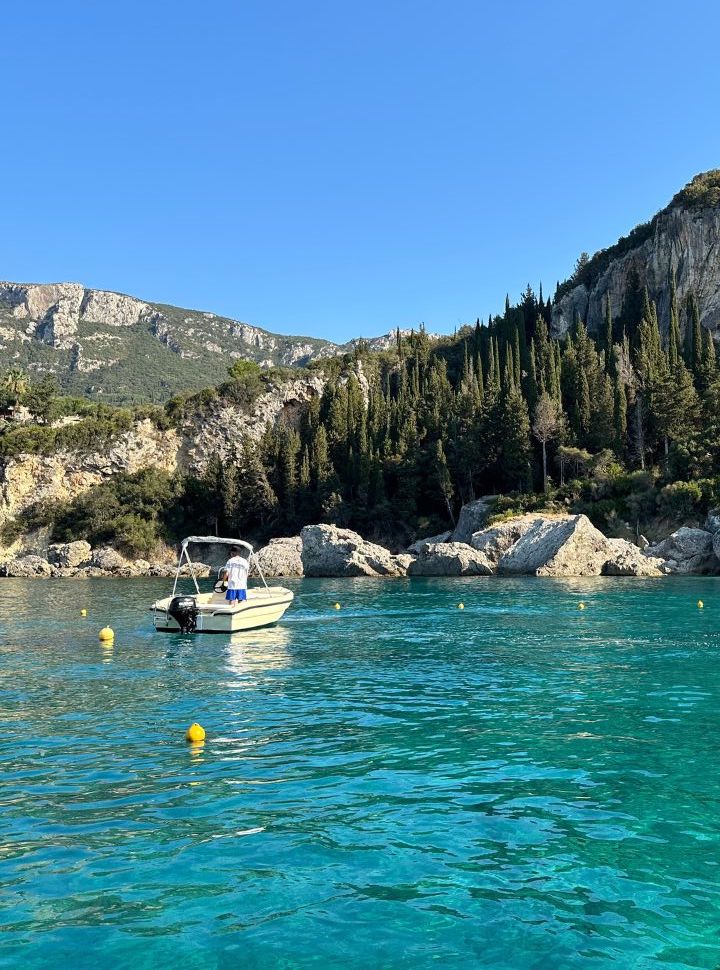 boat floating in the emerald blue water with pine trees the surrounding cliffs at liapedes village