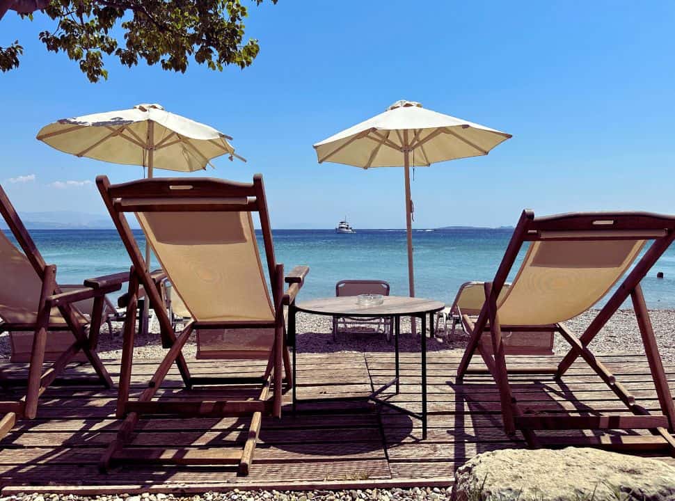 Loungers with sun umbrellas facing a blue ocean on the east coast of Corfu