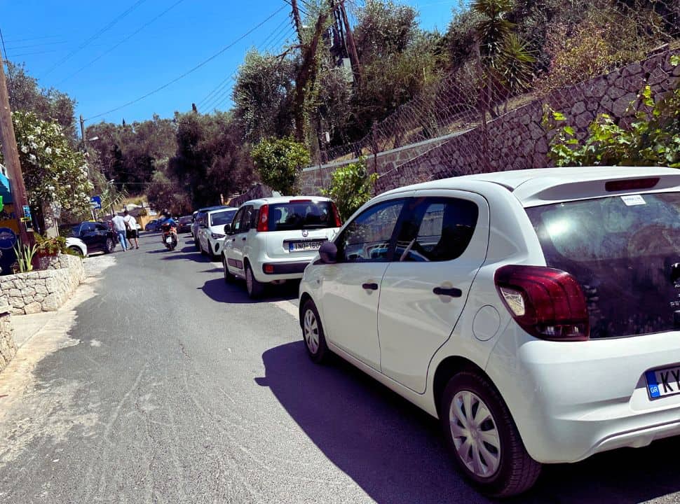 small white cars parked along a narrow road in liapades, a beach town in west corfu