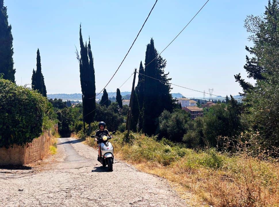 woman driving a motorscooter upill in a green landscape