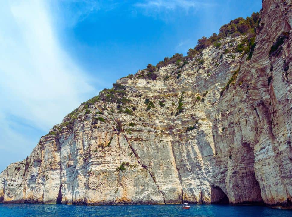 white lime gliffs towering over the blue ocean and little boat near paxos corfu island area