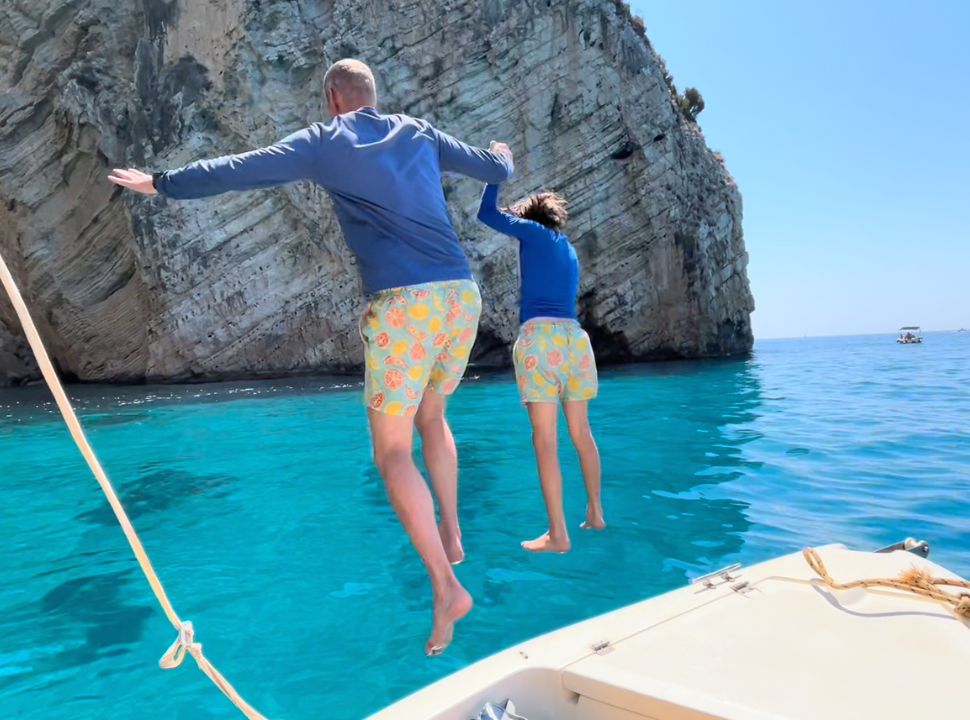 father and son jumping off the boat into the crystal clear blue water