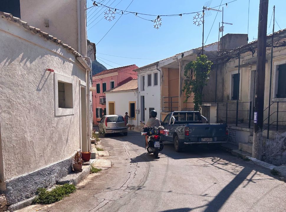 woman driving a motor scooter along a narrow road through a village in corfu