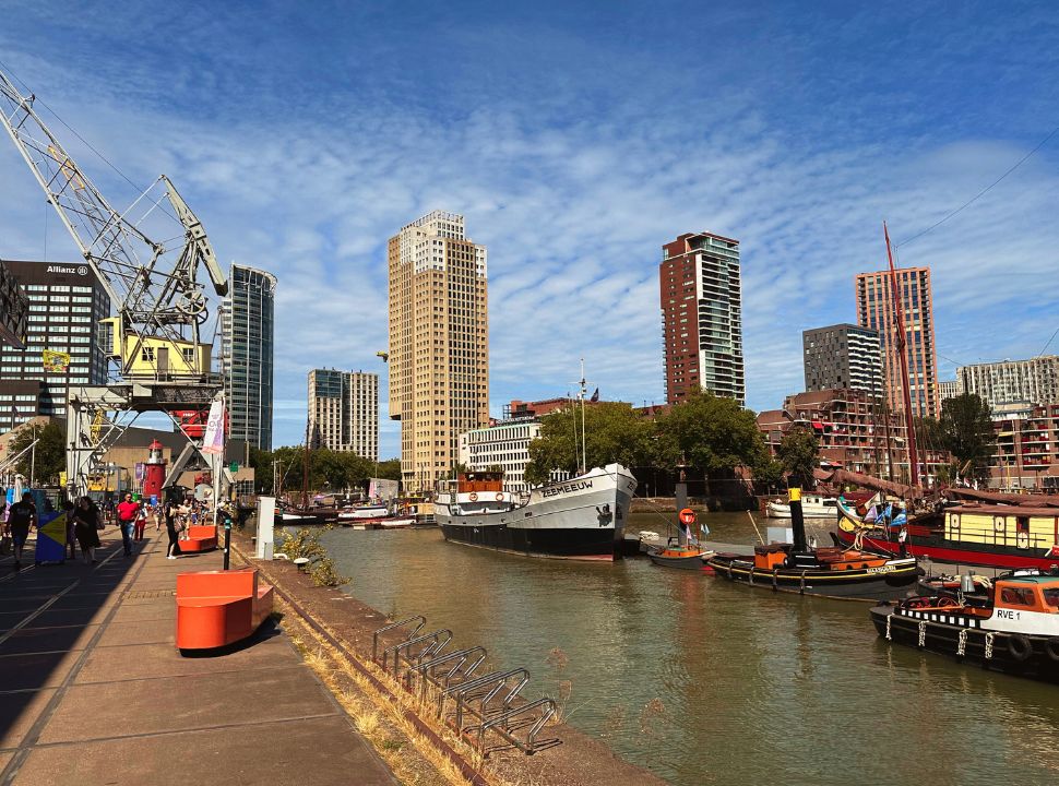 old harbor docks in Rotterdam with a crane and boats with tall buildings in the background