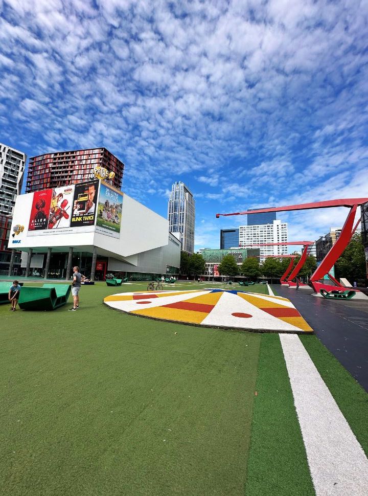 full view of a square with a green carpet, cinema building, and tall buildings in the background