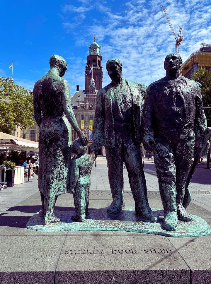 monument of three adults and a child in front of the city hall in Rotterdam