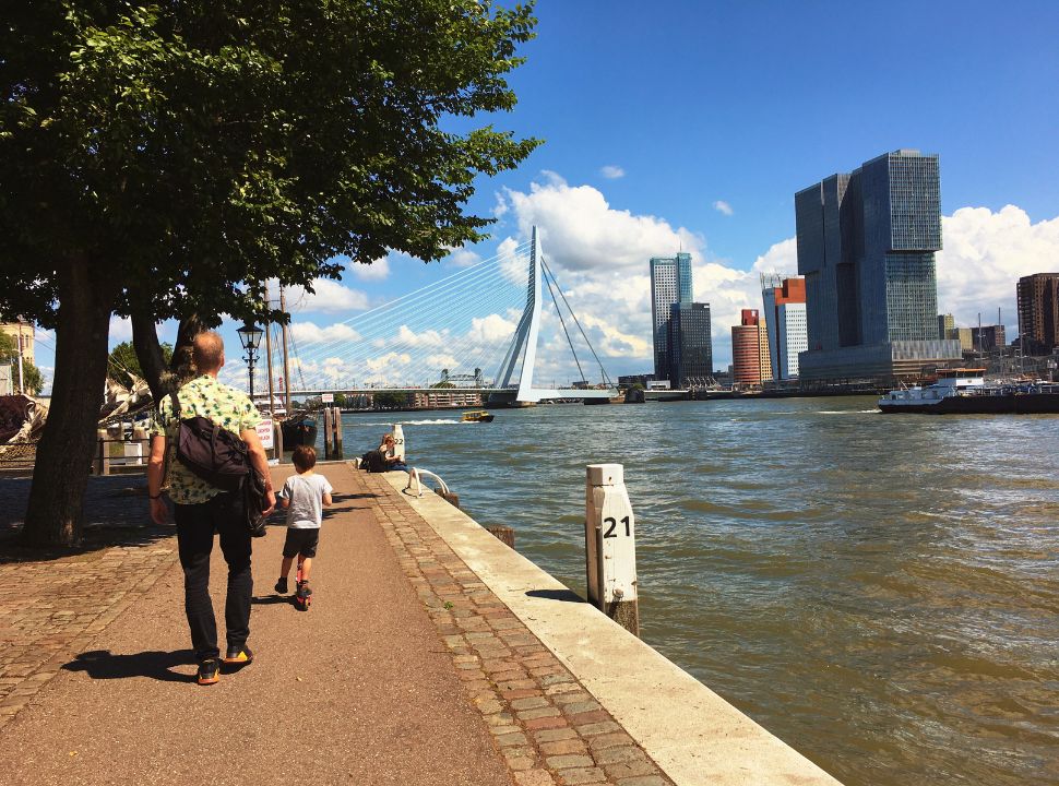 father and son walking along the river front with the erasmus bridge in the distance