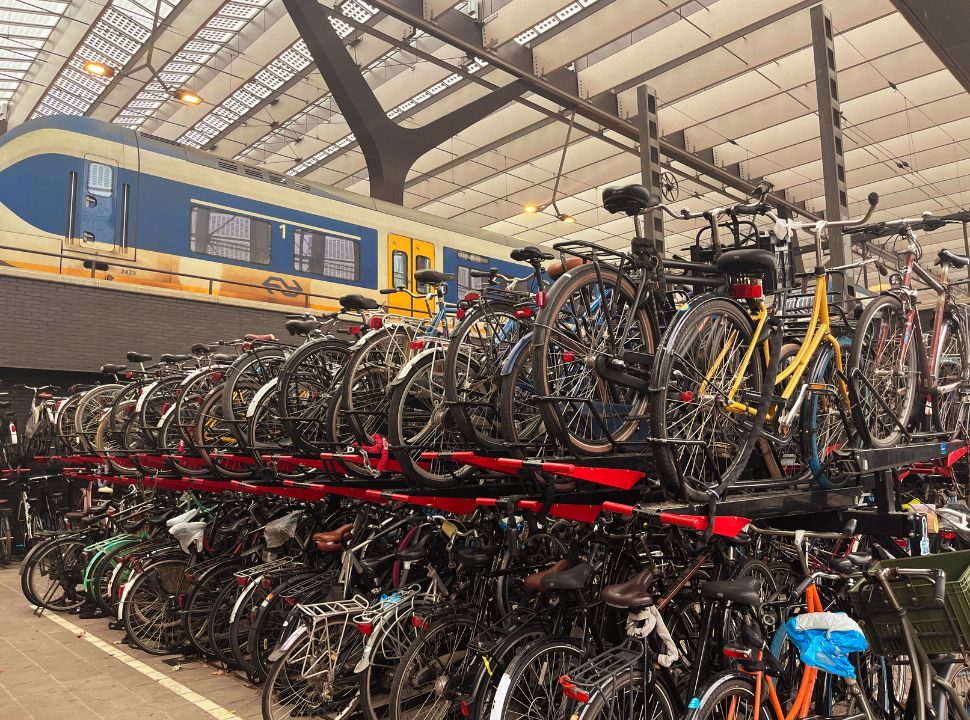 parking stand with many bikes, with the train visible on the back ground at rotterdam train station