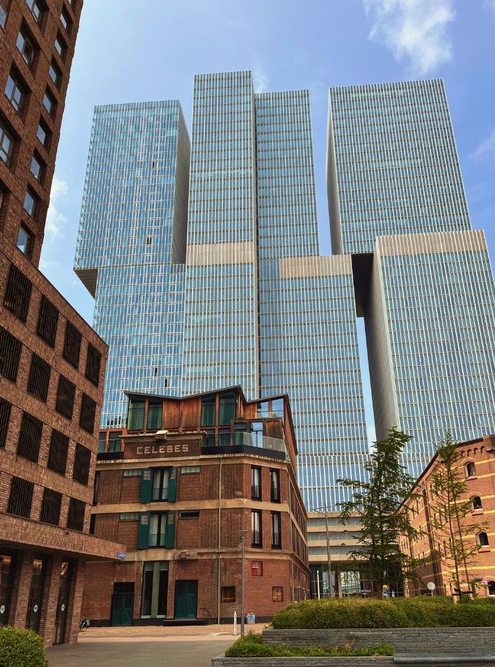 old warehouses stand in front of the tall square stacked building called The Rotterdam