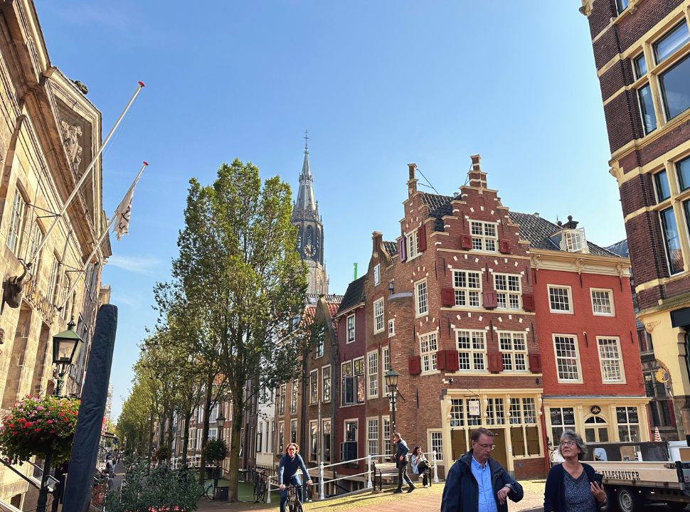 a random corner in delft with a stunning historic building, the tower of the new church, canal and houses. Looks like an open air museum