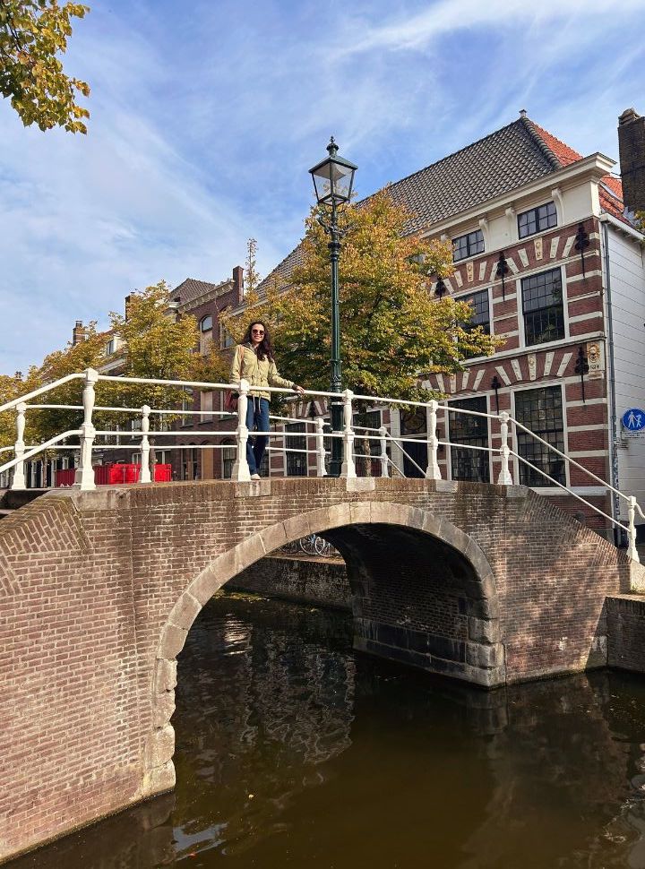 woman standing on a bridge of a old canal in delft with historic buildings in the background