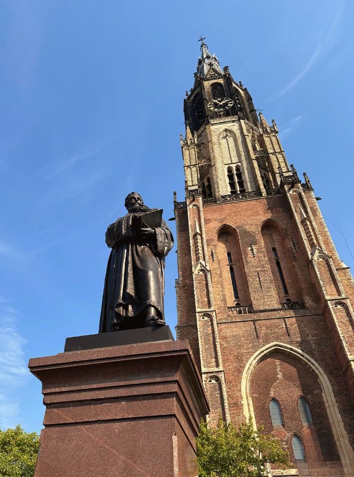 picture looking up to the tower of the nieuwe kerk delft with a statue in front of hugo grotius