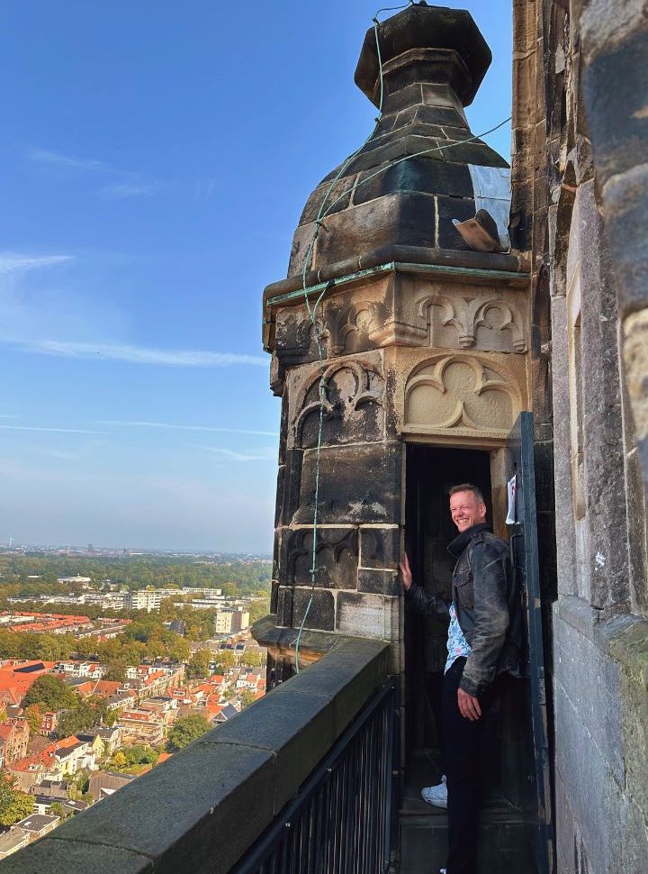 man standing at the doorway of the balcony of the nieuwe kerk balcony with view of delft and beyond