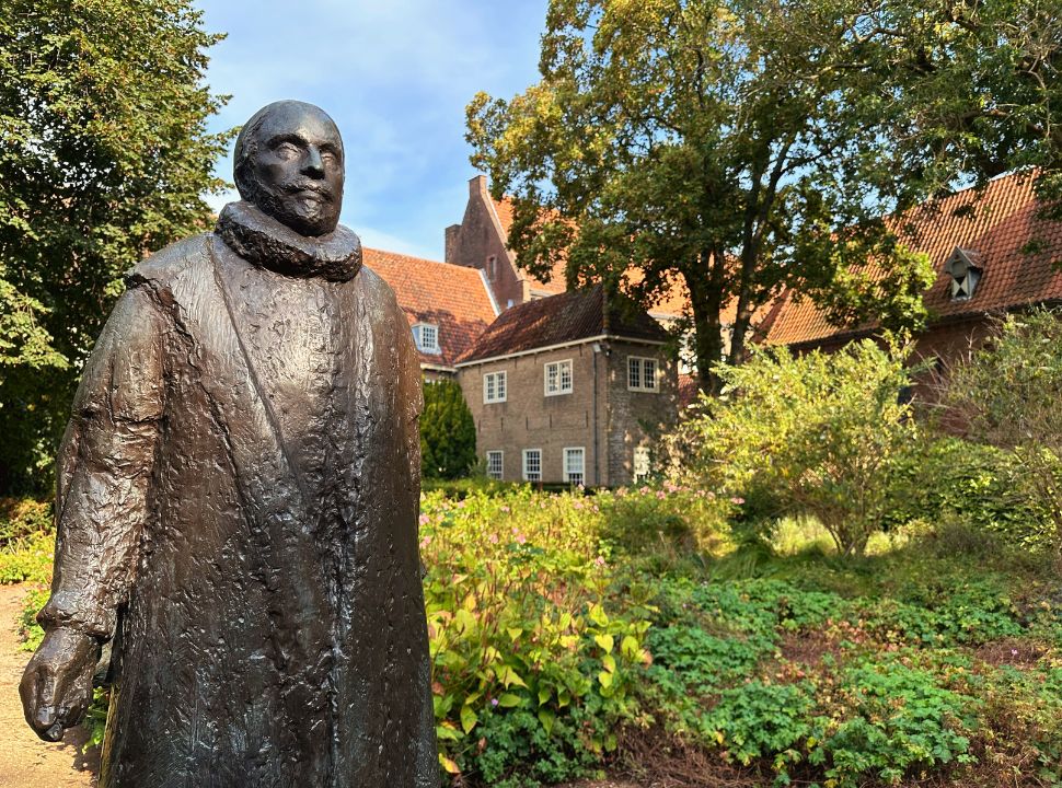 close up statue of Willem of Orange set in a garden with in the back the old monastery and building where he was assassinated