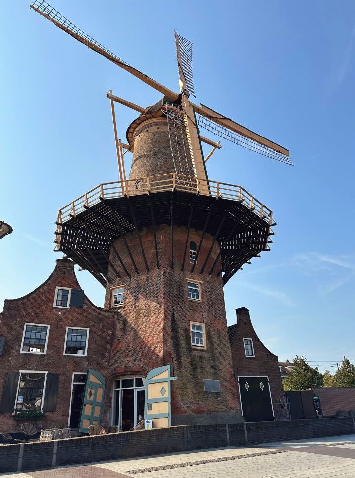 full view of a dutch windmill with its living quarters built around it, doors to the shop is open 