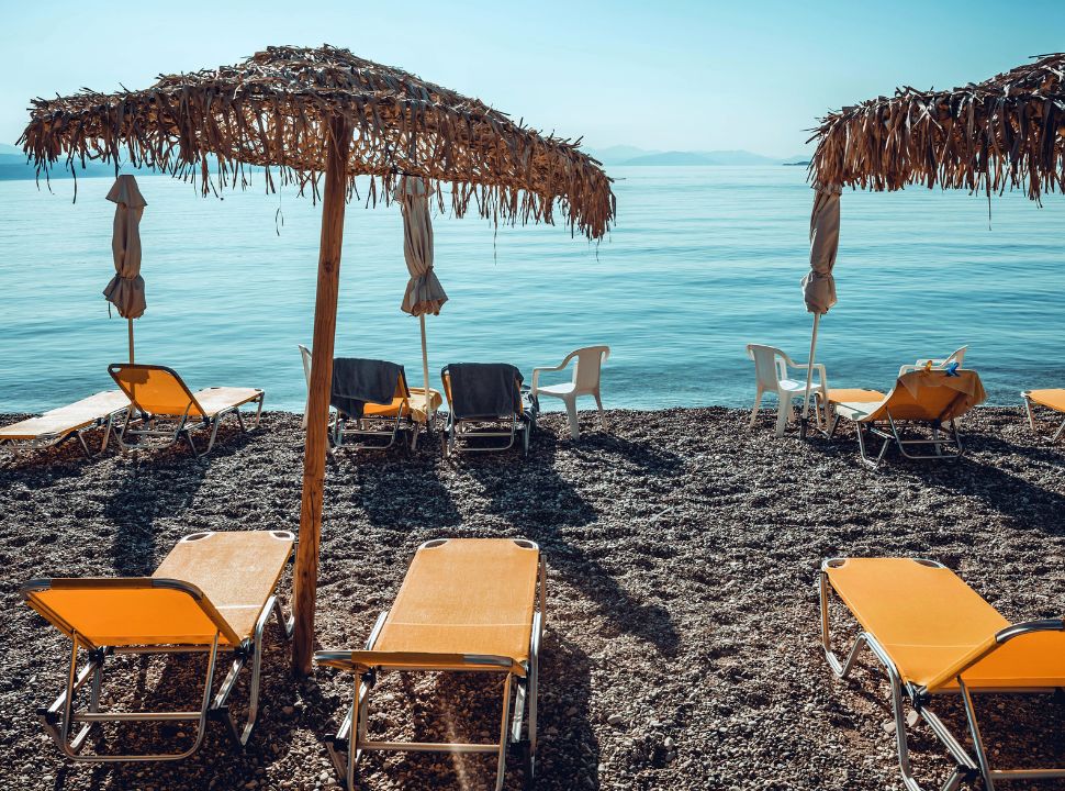 empty sun loungers and umbrellas at a soft pebbled beach with calm water