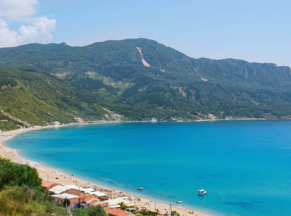 view of a bay with a long stretched beach with stunning blue calm water, sun beds on the beach just as a couple of accommodation options