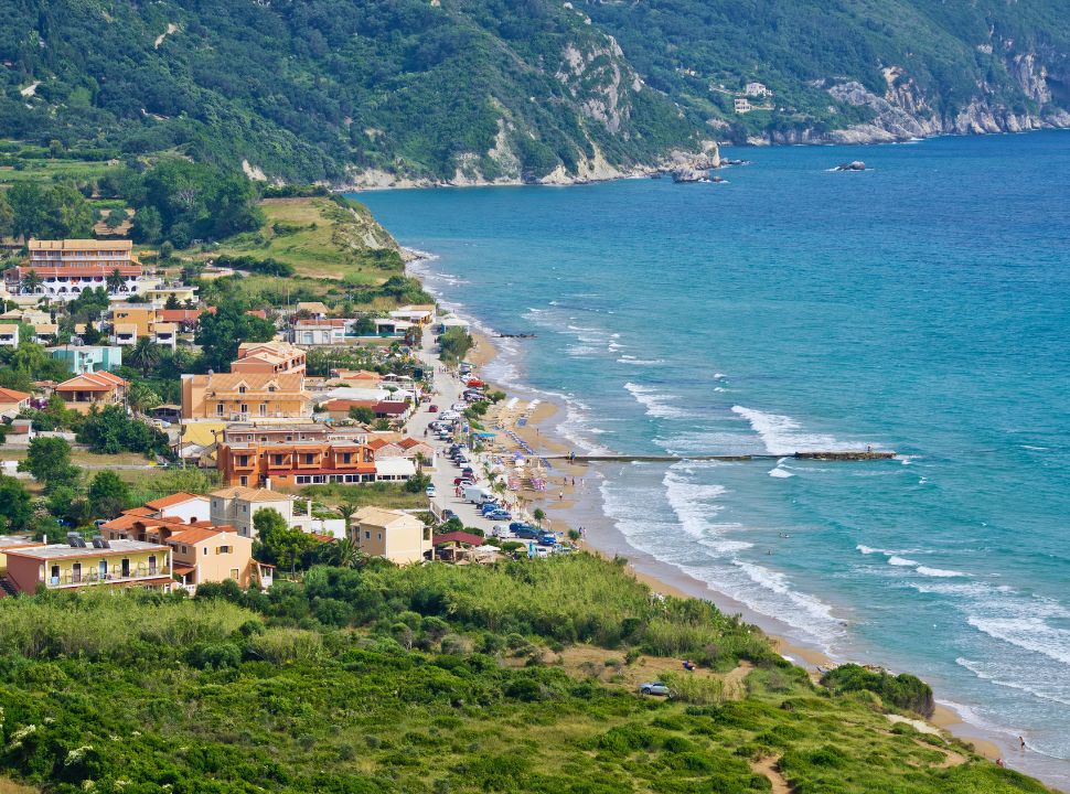 view of a soft sanded beach along a village road, with various types of accommodation. 