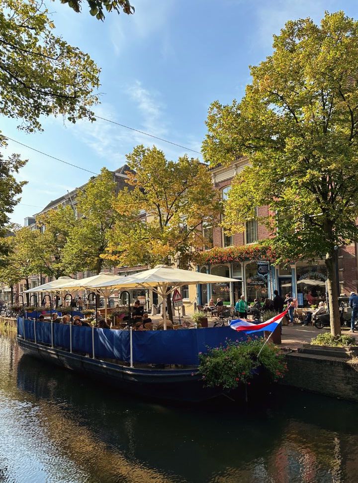 people enjoying lunch on a boat terrace floating in one of the canals in delft