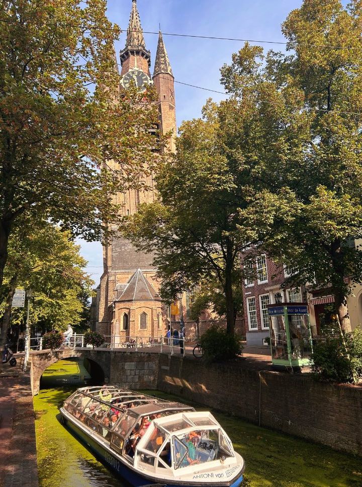 canal tour boat with open glass ceiling, passenger enjoying the tours through the canal with the delft old church in the background