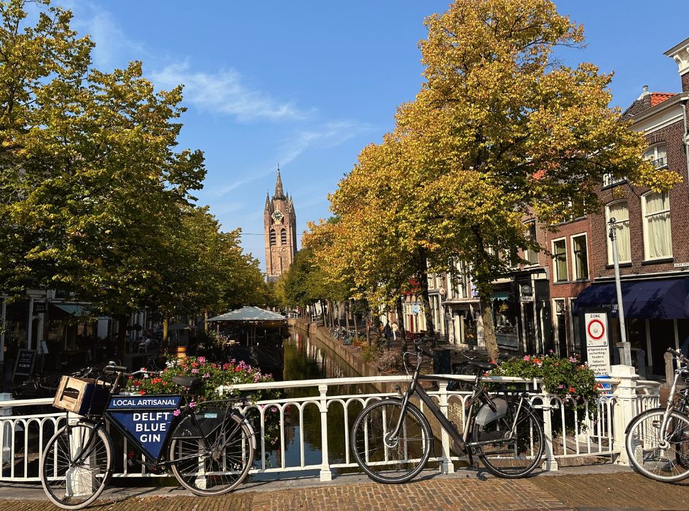 a bridge with bikes parked again the railing, at the end of the canal you can find the leaning tower of the oude kerk in delft