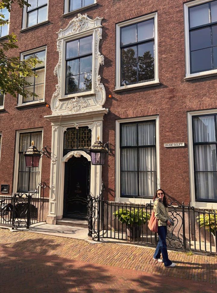 woman walking past a big historical building located along the canal 'oude delft' in the city delft