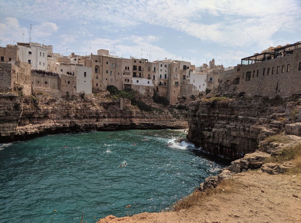 view of the ocean water waves against the cliffs with houses built on the cliff edge, in Polignano a mare Puglia