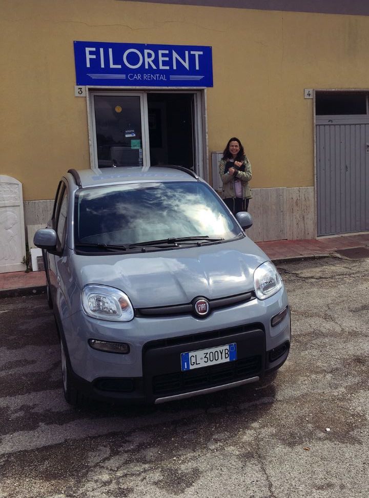 woman standing next to the entrance of a car rental company with a grey car park in front