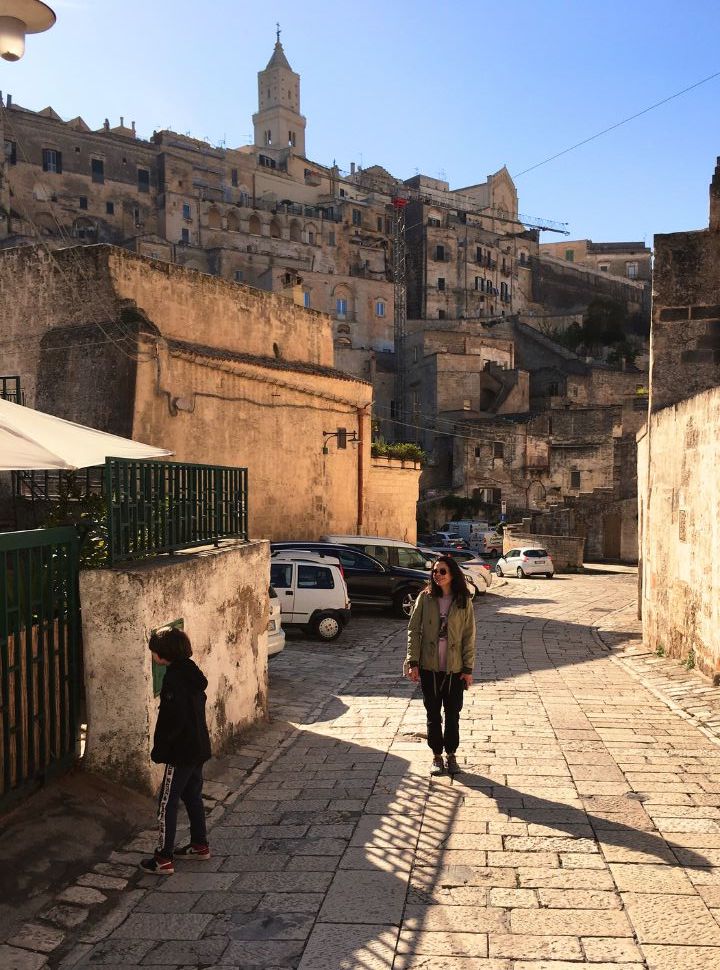 mother and son walking along a street in matera which is accessible by car