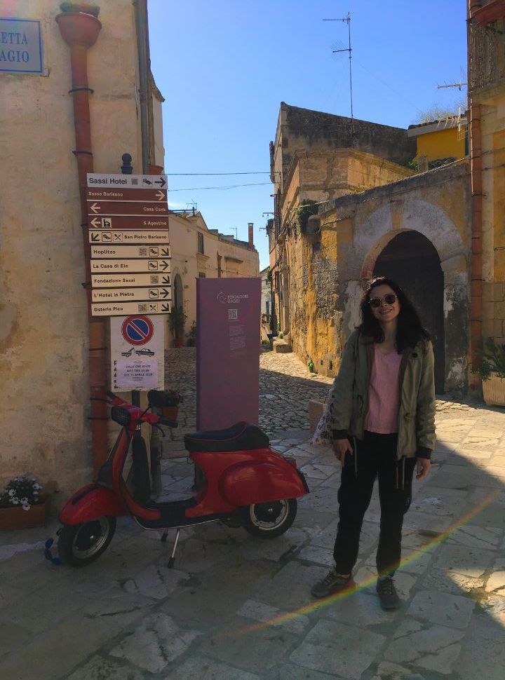 woman standing next to a parked red vespa at one of the many narrow streets of Matera Italy