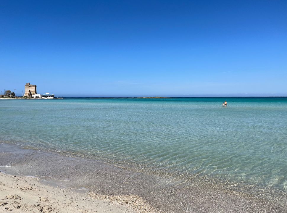 mother and son wading into the shallow ocean water at spaiggia sant'isidoro puglia italy