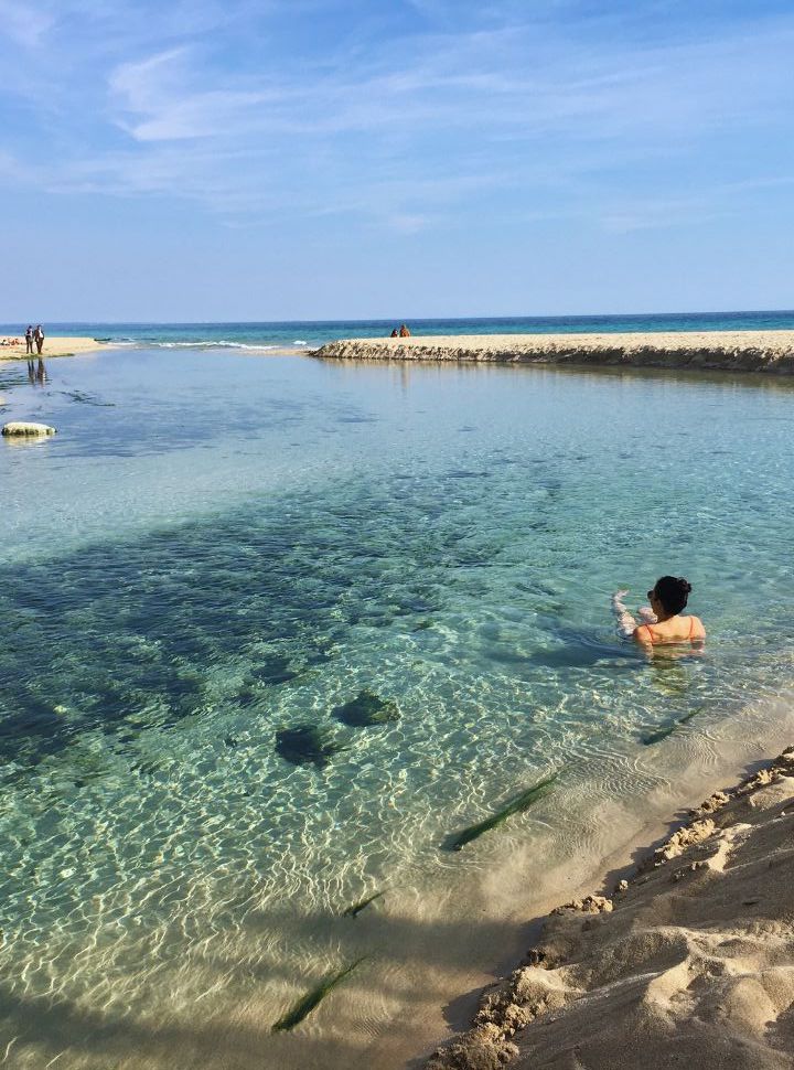 woman enjoying the clear fresh water that flows into the salty ocean at Spiaggia del Chidro Puglia