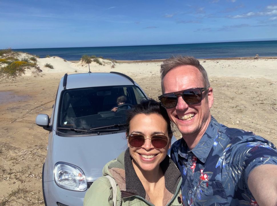 couple posing in front of their rental car at a beach in Puglia Italy